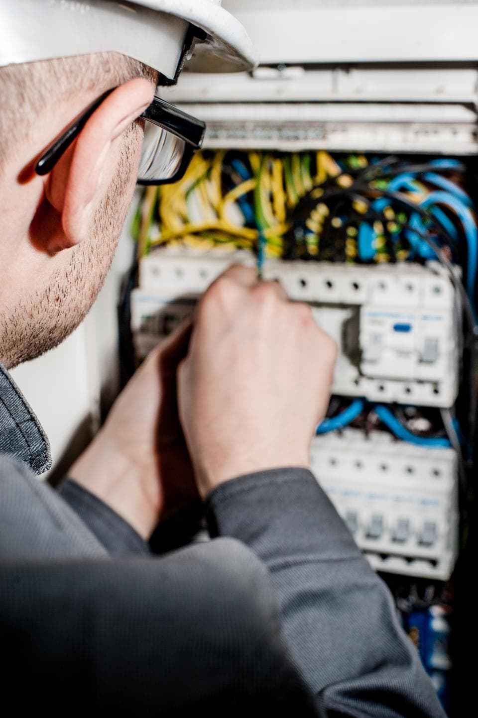 An electrician in a hard hat and safety glasses wiring a residential switchboard